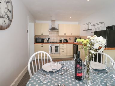 A kitchen with cream cabinets stove and dining table with wine and flowers at The Linhay in Chardstock