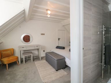 A bedroom with a gray ottoman bench and dressing table next to a bathroom at The Linhay in Chardstock