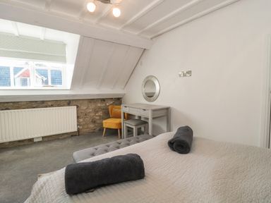 A bedroom with a bed rolled towels a desk a stool a yellow chair a radiator and a window at The Linhay in Chardstock