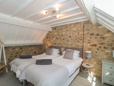 A bedroom with two single beds stone wall slanted ceiling and bedside table with lamp at The Linhay in Chardstock