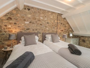 A bedroom with two single beds bedside tables and lamps against a stone wall at The Linhay in Chardstock