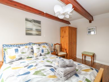 A bedroom with a double bed with colorful bedding towels stacked on the bed wooden wardrobe chair and small checkered stool at Compass Cottage Bodham near Sheringham