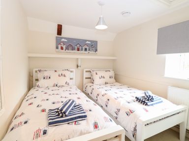 A bedroom with two single beds with nautical themed bedding and folded striped towels on top at Compass Cottage in Bodham near Sheringham