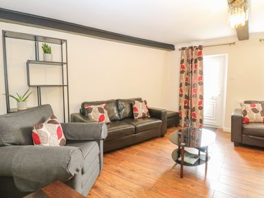 A living room with sofas coffee table shelves and patterned curtains at Compass Cottage in Bodham near Sheringham