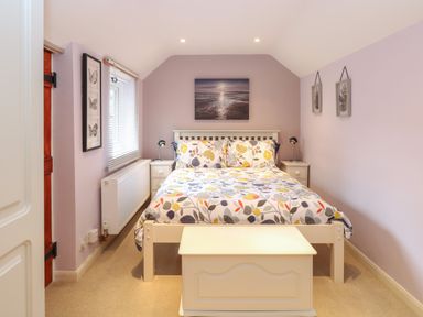 A bedroom with a bed and floral bedding two bedside tables with lamps a chest at the foot of the bed and framed pictures on the walls at Compass Cottage Bodham near Sheringham