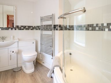 A bathroom with a toilet sink cabinet towel radiator and bathtub at Compass Cottage in Bodham near Sheringham
