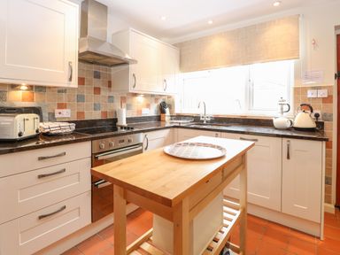 A kitchen with white cabinets a wooden island a toaster a kettle and a window at Compass Cottage in Bodham near Sheringham