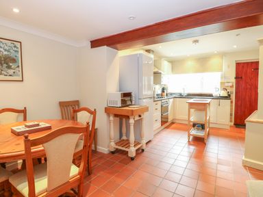 A kitchen and dining area with wooden chairs and table a microwave on a small cart a refrigerator a kitchen island and cabinets at Compass Cottage Bodham near Sheringham