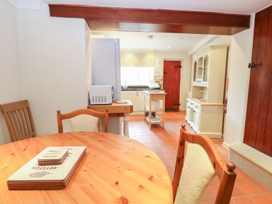 A kitchen with a round wooden table and chairs a microwave on a small table a kitchen island cupboards and a red wooden door at Compass Cottage in Bodham near Sheringham
