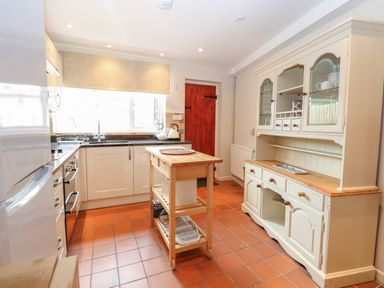 A kitchen with white cabinets a wooden island and a cupboard at Compass Cottage in Bodham near Sheringham