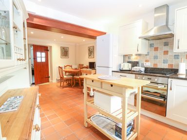 A kitchen and dining area with a wooden island, white cabinets, tiled floor, and a dining table with chairs at Compass Cottage in Bodham near Sheringham