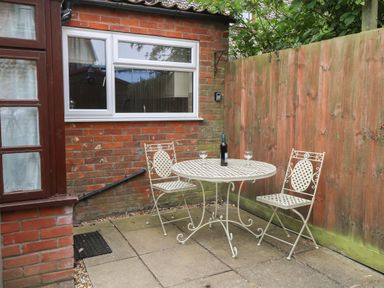An outdoor patio area with a round metal table and two chairs a bottle and two glasses on the table at Compass Cottage Bodham near Sheringham