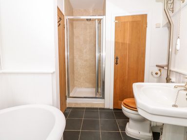 A bathroom with a bathtub a shower cubicle a toilet with a wooden seat and a white sink at Puffin Cottage in Hawkchurch