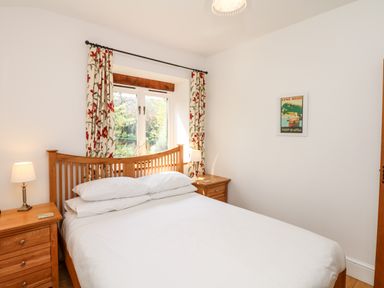 A bedroom with a wooden bed and two bedside tables with lamps at Puffin Cottage in Hawkchurch