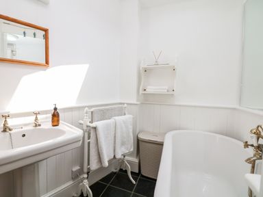 A bathroom with a sink towels on a rack a laundry basket and a bathtub at Puffin Cottage in Hawkchurch