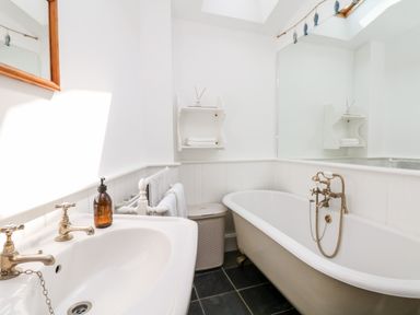 A bathroom with a bathtub a sink a mirror a towel rack and a shelf with towels at Puffin Cottage in Hawkchurch