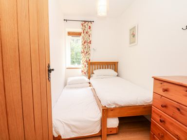 A small bedroom with two single beds a wooden chest of drawers and a window with floral curtains at Puffin Cottage in Hawkchurch