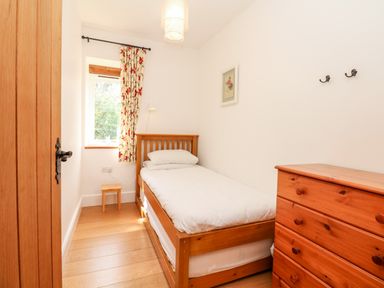 A small bedroom with a single bed wooden chest of drawers and a window with floral curtains at Puffin Cottage in Hawkchurch