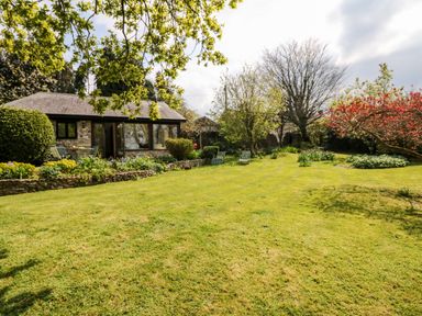 A garden with lawn chairs trees and a small stone building at Puffin Cottage in Hawkchurch