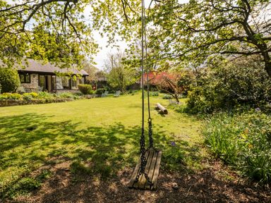 A garden with a wooden swing and chairs near a stone cottage at Puffin Cottage in Hawkchurch
