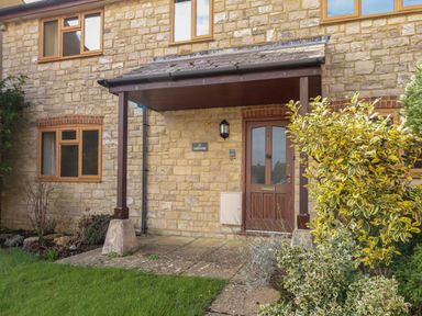 The front entrance of a stone house with a brown door and a small porch at Gabrianne in Burton Bradstock