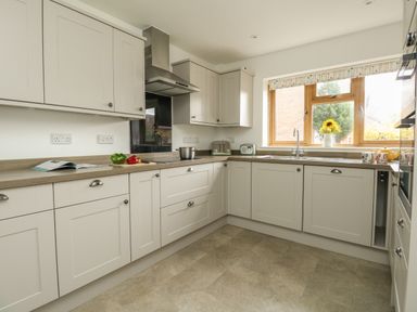 A kitchen with white cabinets a pot on the stove a toaster and a vase with sunflowers on the windowsill at Gabrianne in Burton Bradstock