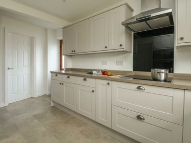 A kitchen with white cabinets a stovetop with a pot and a countertop with vegetables and a magazine at Gabrianne in Burton Bradstock