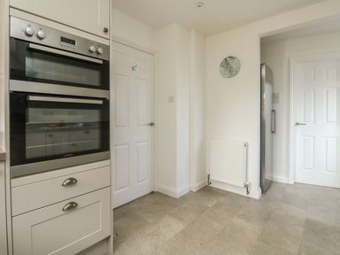 A kitchen area with built in double oven two white doors a radiator and a stainless steel fridge at Gabrianne Burton Bradstock