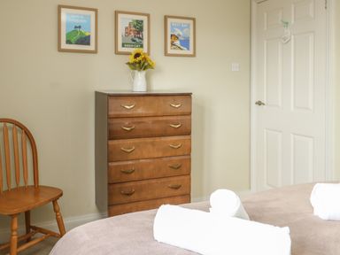 A bedroom with a wooden dresser with a vase of sunflowers a wooden chair a white door and a bed with rolled white towels at Gabrianne Burton Bradstock