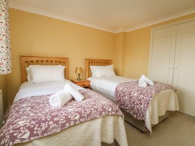 A bedroom with two single beds a bedside table with a lamp and a built-in wardrobe at Gabrianne in Burton Bradstock