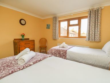 A bedroom with two single beds a wooden chest of drawers a chair and a window with patterned curtains at Gabrianne in Burton Bradstock