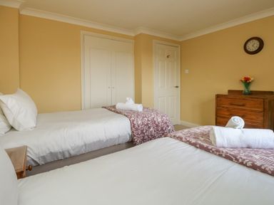 A bedroom with two single beds white linens folded towels on beds wooden chest of drawers with flowers clock on wall at Gabrianne in Burton Bradstock