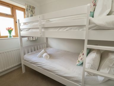 A bedroom with a white bunk bed with pillows and towels near a window with curtains at Gabrianne in Burton Bradstock