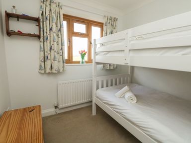 A bedroom with white bunk beds a wooden window with patterned curtains and a vase of flowers at Gabrianne in Burton Bradstock