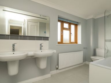 A bathroom with two sinks a toilet a bathtub a window and a radiator at Gabrianne in Burton Bradstock