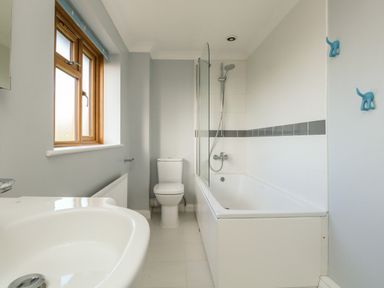 A bathroom with a bathtub and shower, a toilet, a sink, and a window at Gabrianne in Burton Bradstock