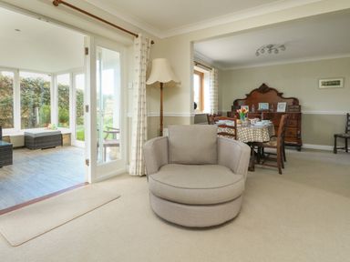 A living room with a round chair a floor lamp a dining table and chairs and a glass door leading to a sunroom at Gabrianne in Burton Bradstock