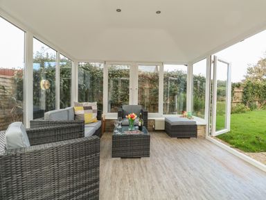 A sunroom with wicker furniture and glass doors leading to a garden at Gabrianne in Burton Bradstock