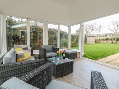 A sunroom with wicker furniture a glass coffee table and a view of a garden at Gabrianne Burton Bradstock