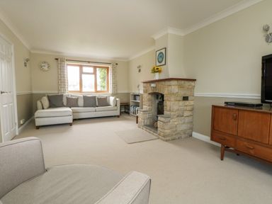 A living room with a stone fireplace a large sofa a wooden sideboard and a window with curtains at Gabrianne in Burton Bradstock