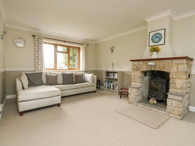 A living room with a beige sofa under a window a stone fireplace and a small bookshelf at Gabrianne in Burton Bradstock