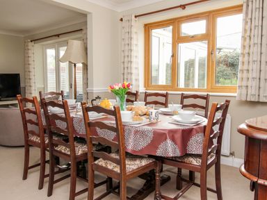 A dining room with a table set for a meal and wooden chairs near a window at Gabrianne in Burton Bradstock
