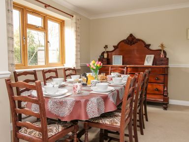 A dining room with a table set for breakfast and wooden chairs near a wooden sideboard at Gabrianne Burton Bradstock