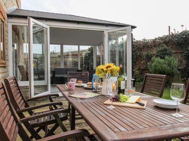 A wooden outdoor dining table with chairs and various items on it in a garden at Gabrianne in Burton Bradstock