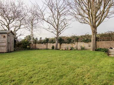A garden with green grass trees a wooden shed and a wooden fence with plants at Gabrianne in Burton Bradstock