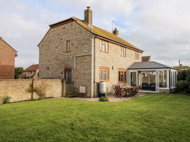 A stone house with a garden table and chairs on a patio next to a glass conservatory at Gabrianne in Burton Bradstock