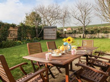 A wooden table with cups plates muffins and flowers in a garden with wooden chairs at Gabrianne Burton Bradstock
