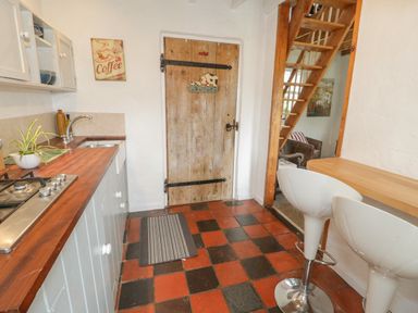 A kitchen with a wooden countertop sink gas stove two white bar stools a wooden door and stairs at Little House in Red Wharf Bay