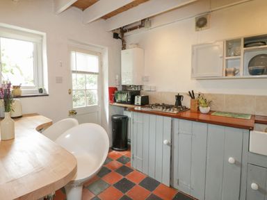 A kitchen with a wooden countertop and gas stove with white cabinets and a tiled floor at Little House in Red Wharf Bay