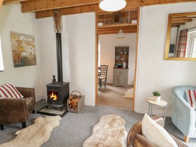 A living room with a wood burning stove chairs rugs and a view into a dining area at Little House in Red Wharf Bay